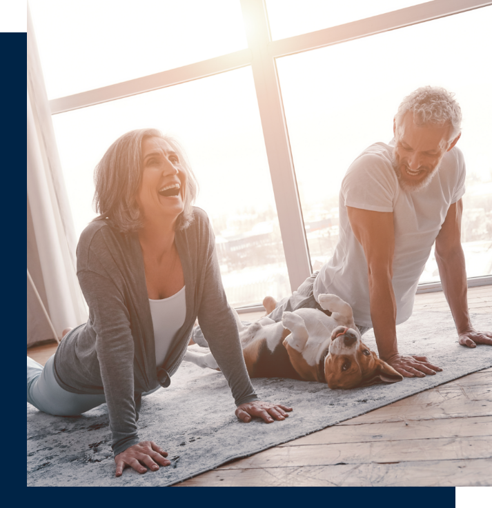 Older couple doing yoga and laughing with their puppy who is trying to join in with them